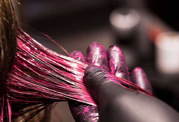 Close-up view of a gloved hand coating hair in bright pink hair dye