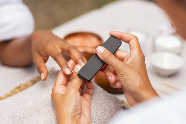 A close-up view of a nail technician filing a client's nails.